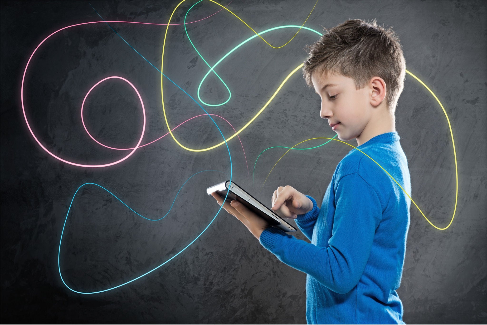 Un enfant se tient de profil, tenant une tablette avec des lignes colorées.