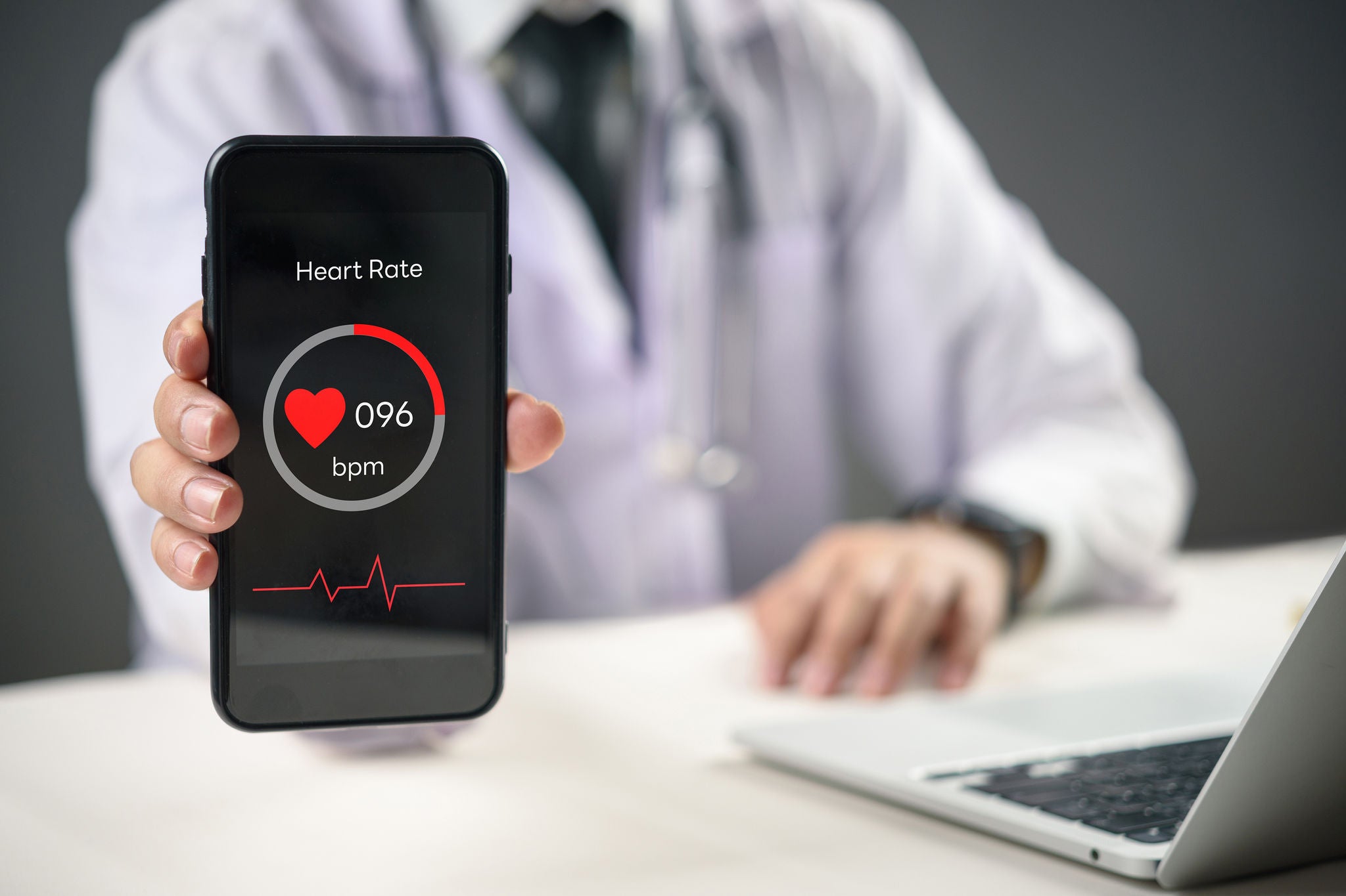 Person holding smartphone showing heart rate reading at desk